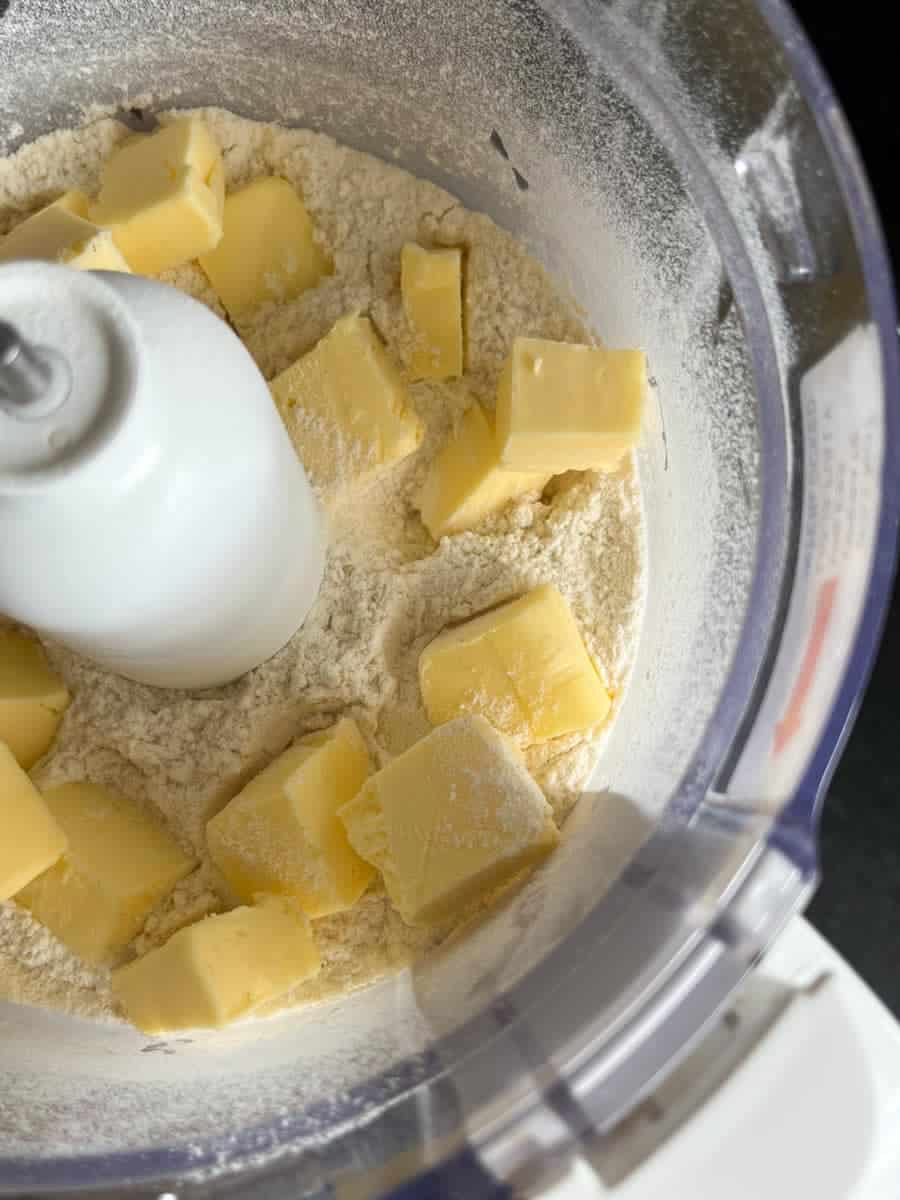 Flour and cubed butter inside the bowl of a food processor.