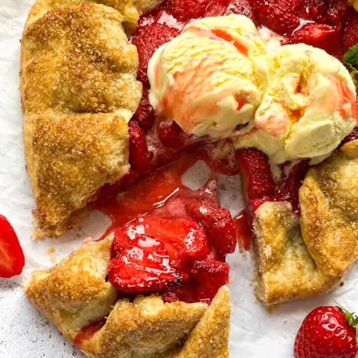 A strawberry galette topped with vanilla ice cream and drizzled with strawberry sauce on a piece of baking parchment.