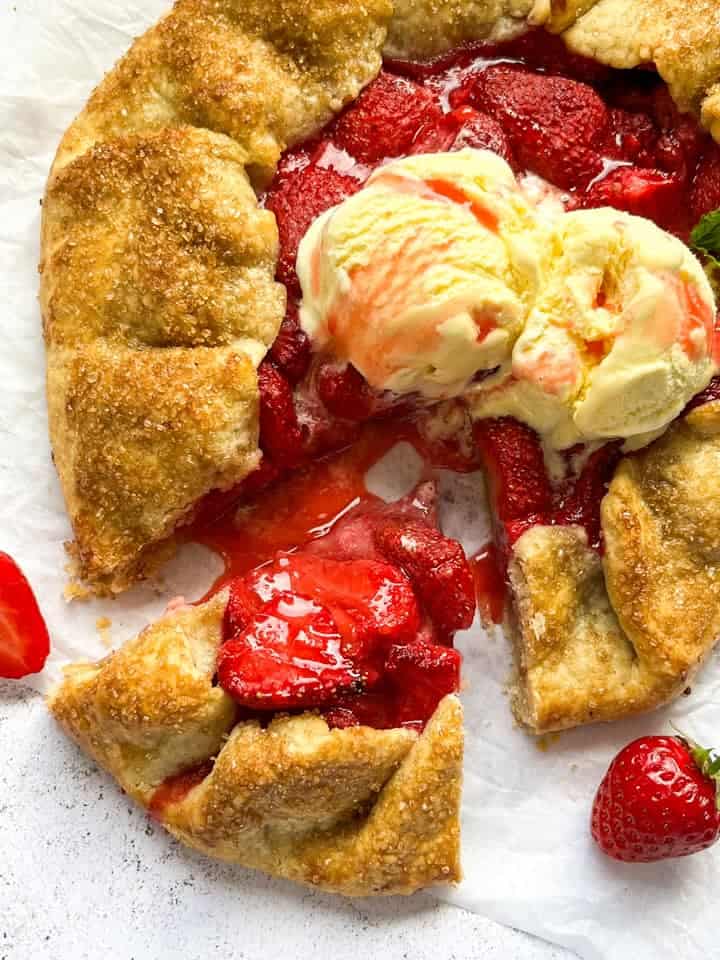 A strawberry galette topped with vanilla ice cream and drizzled with strawberry sauce on a piece of baking parchment.
