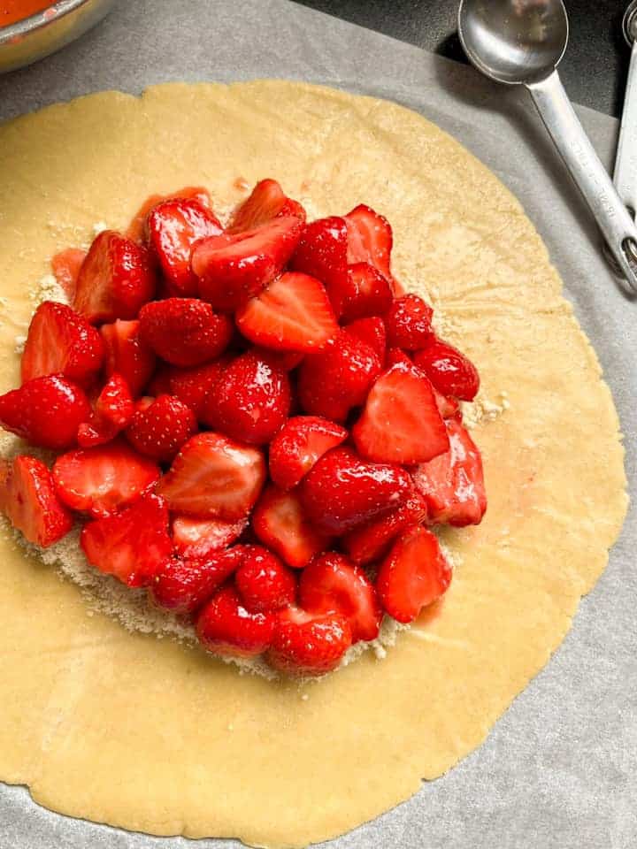 A circle of rolled out pie dough on a piece of baking parchment topped with ground almonds and fresh strawberries.