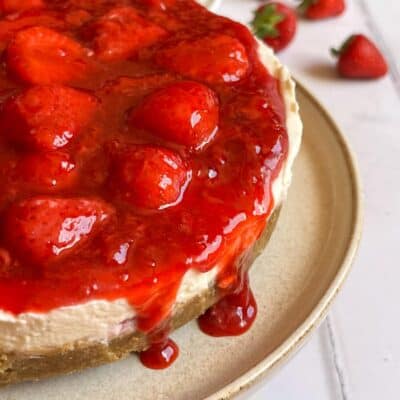 A no bake cheesecake topped with fresh strawberry compote on a beige plate.