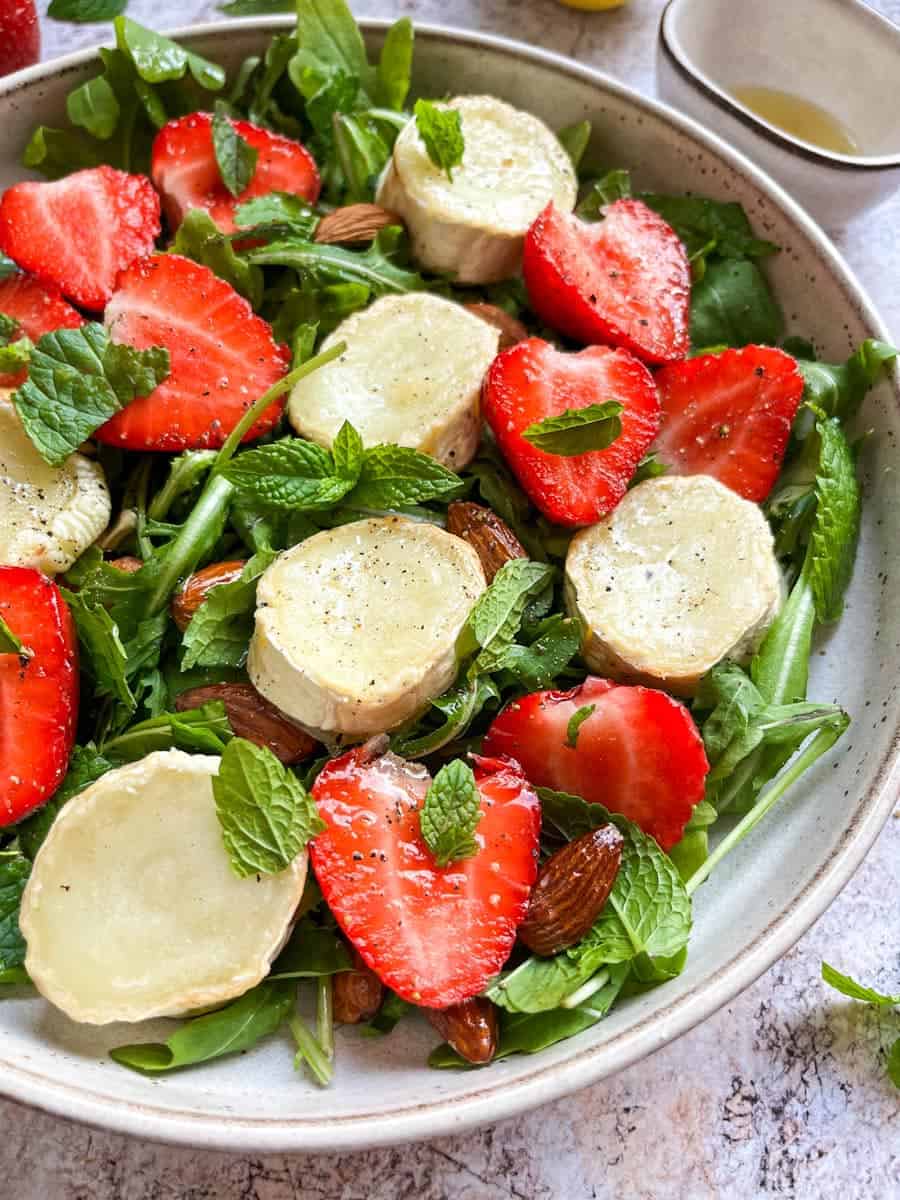 A rocket salad with sliced goat's cheese, strawberries, almonds and fresh mint leaves.