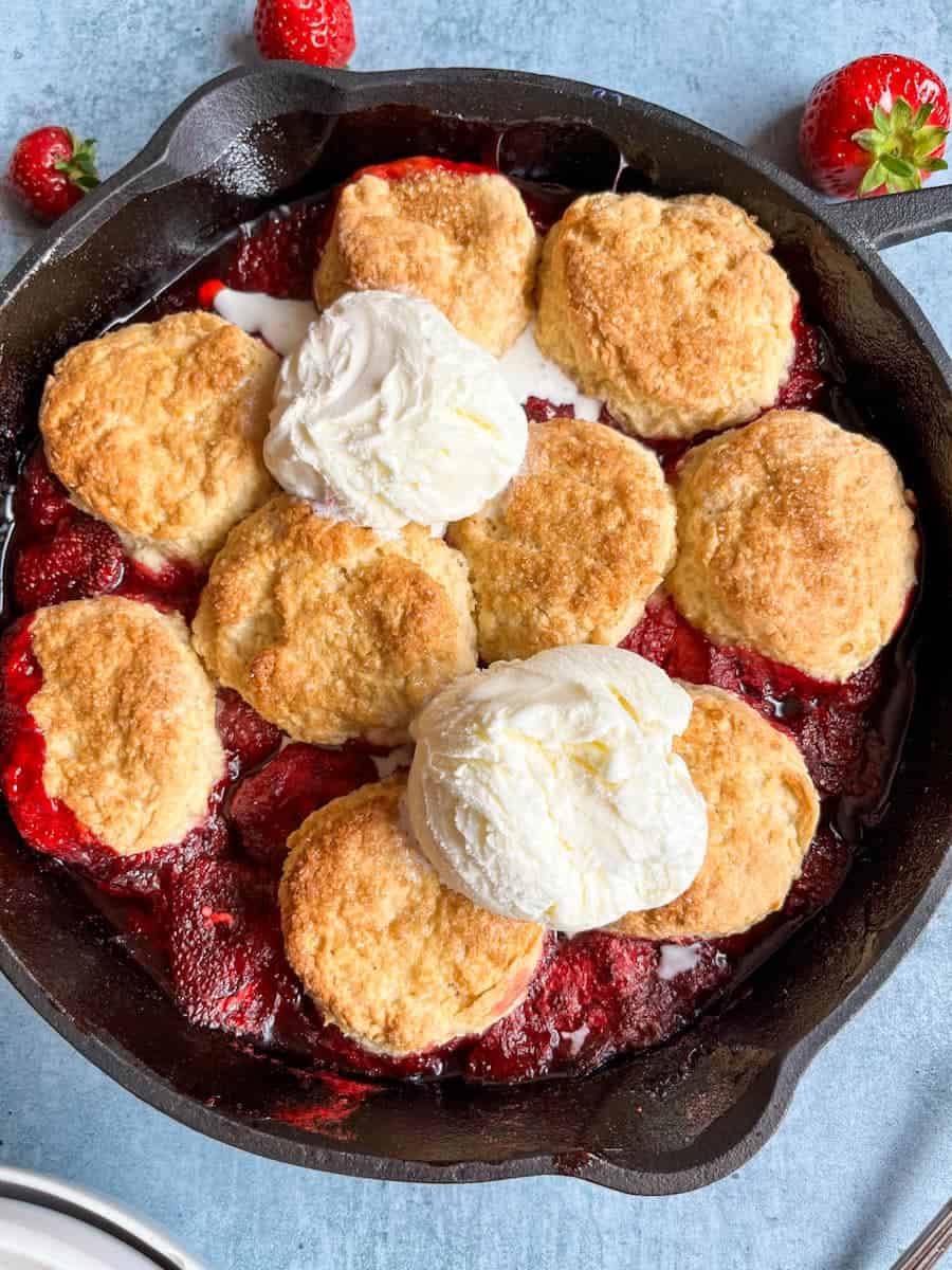 A strawberry cobbler topped with two scoops of vanilla ice cream in a black skillet.