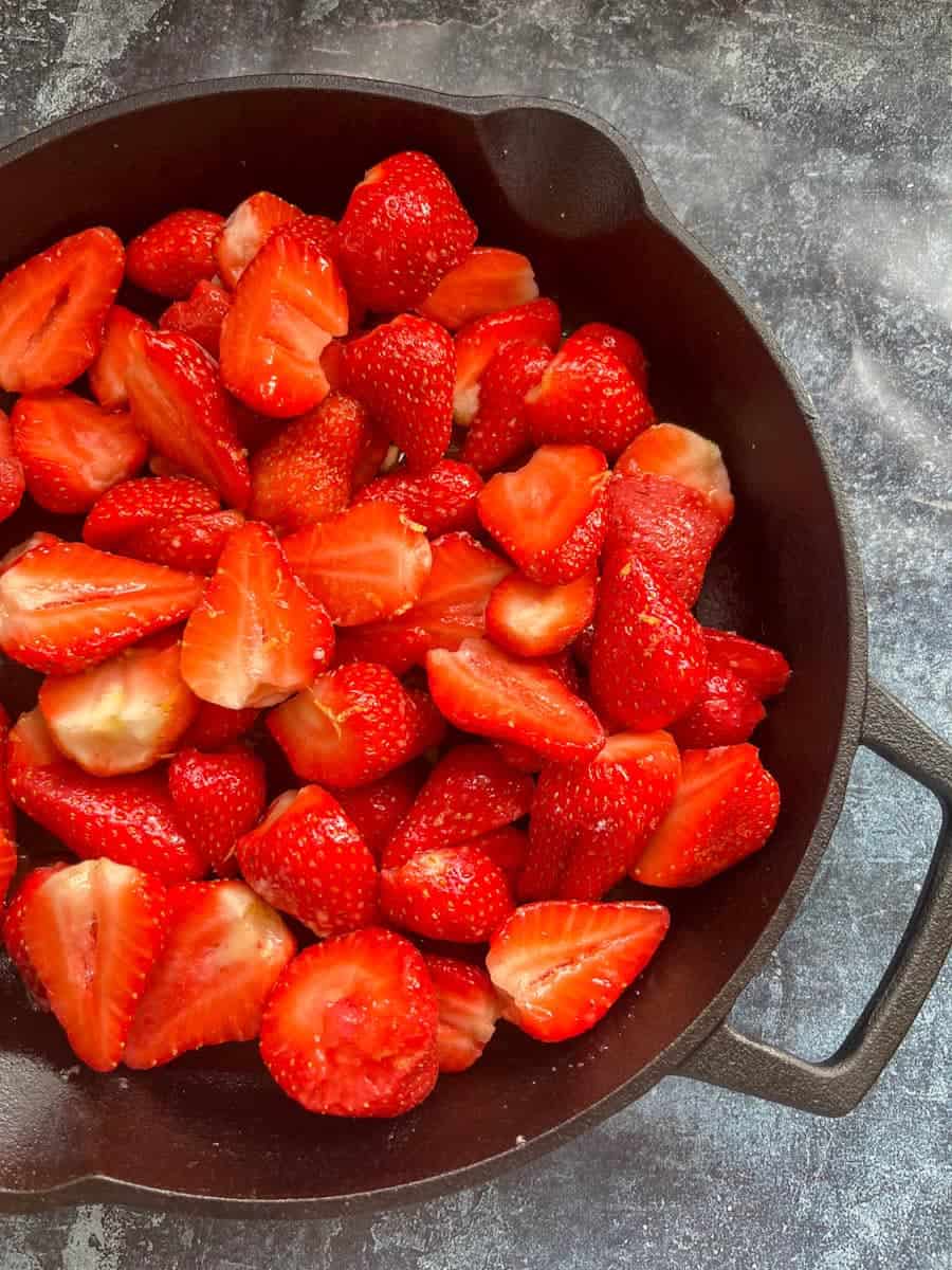 A black skillet filled with fresh halved strawberries.