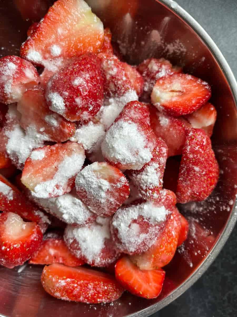 A silver bowl of halved strawberries sprinkled with cornflour.