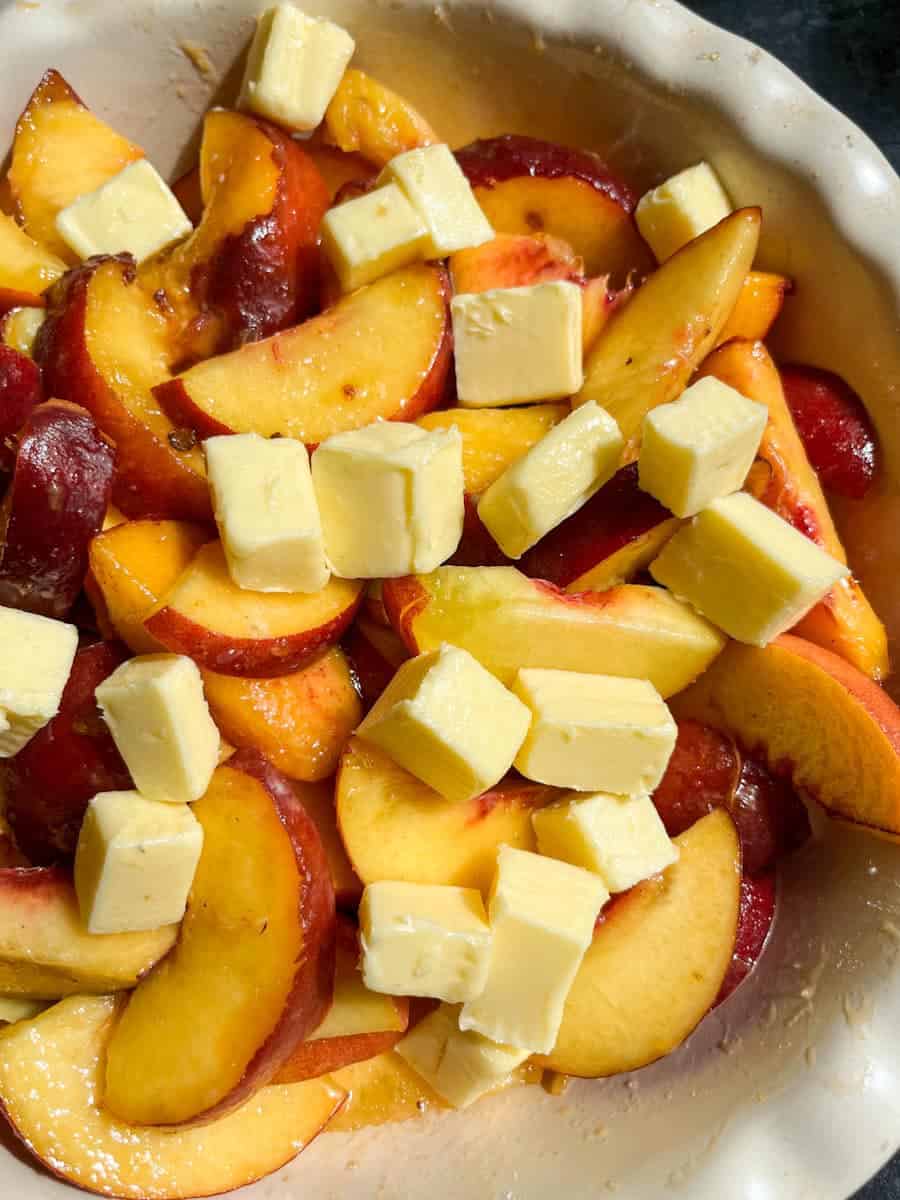 A pie dish filled with fresh sliced peaches and cold diced butter.