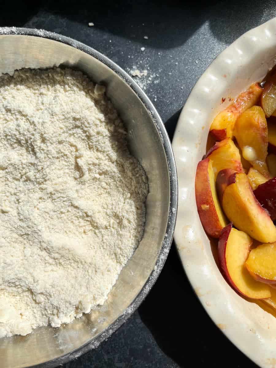 A silver bowl of flour and a white pie dish filled with sliced peaches.