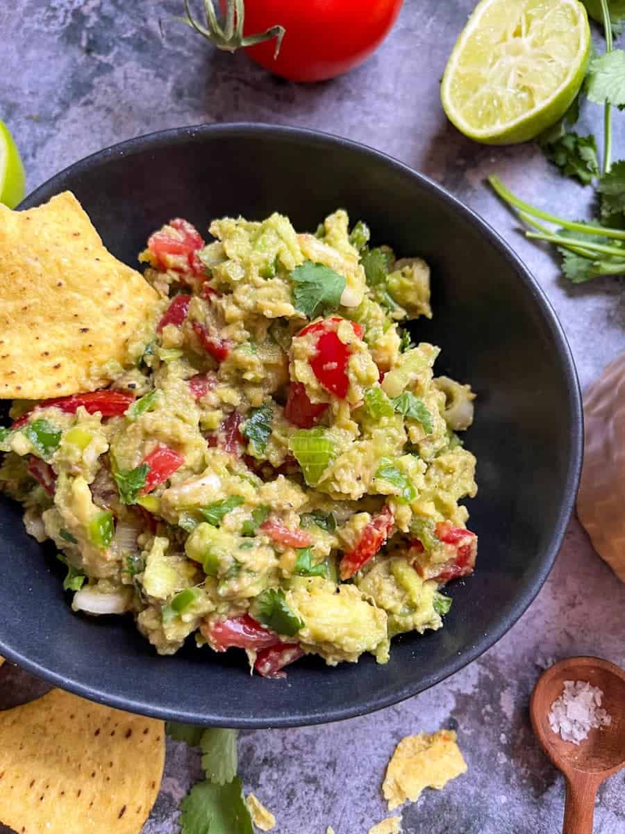 A black bowl of Guacamole with chopped tomatoes and spring onions. 