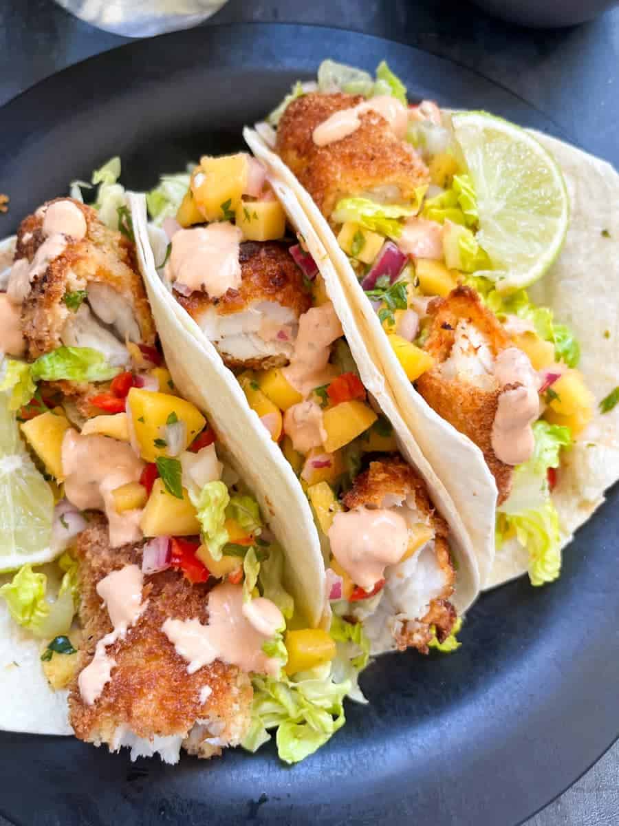 three tacos with breadcrumbed fish fillets, cubed mango, red onion, shredded lettuce and drizzled with chipotle sauce.