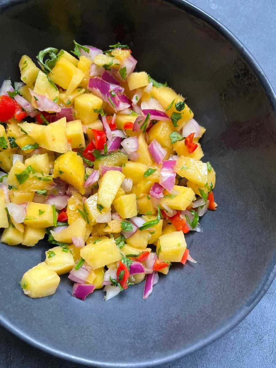 A black bowl of diced mango, chopped red chilli, diced red onion and chopped coriander.