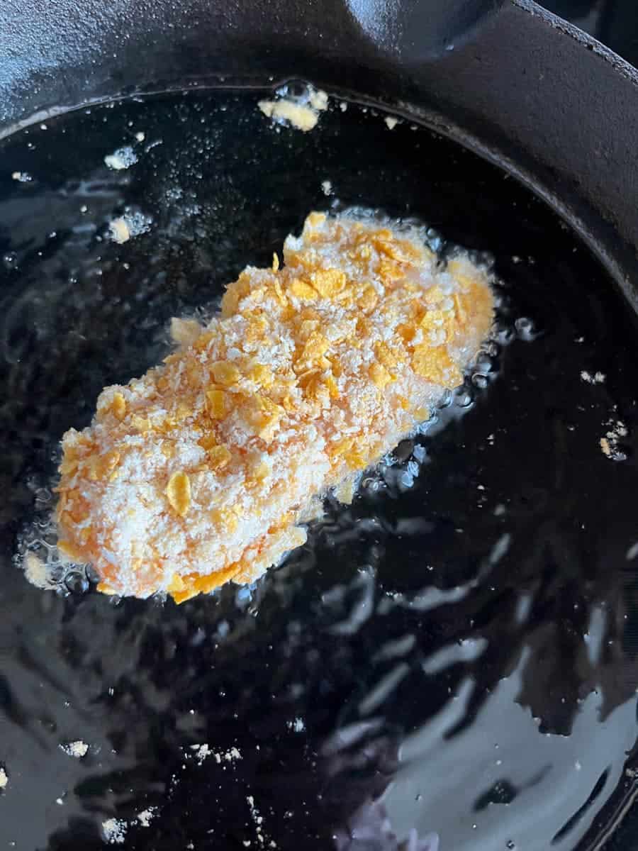 A fish finger in cornflakes frying in a pan of oil.