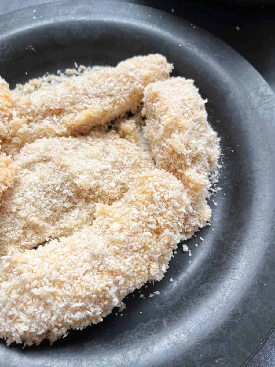 a black plate of raw breaded fish fingers.