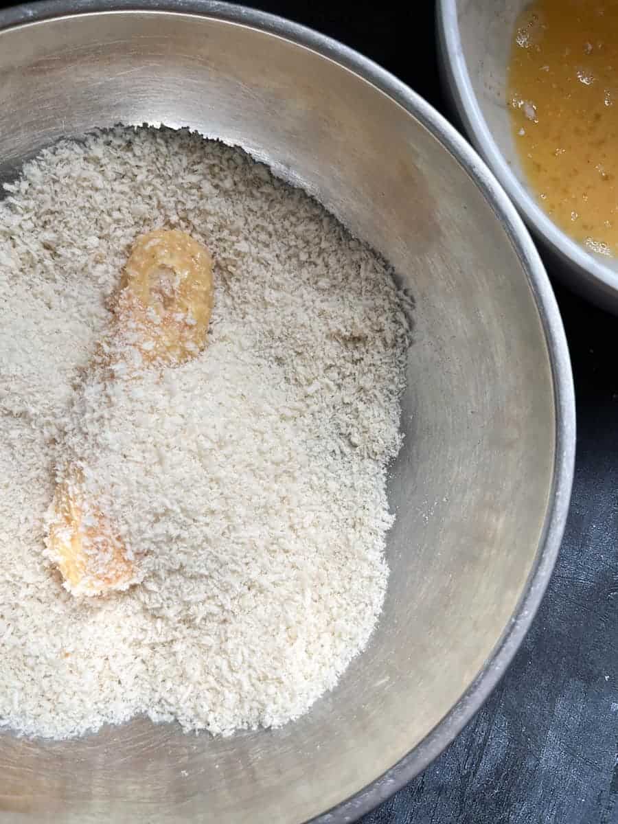 a fish finger in a bowl of panko breadcrumbs and a bowl of beaten egg.