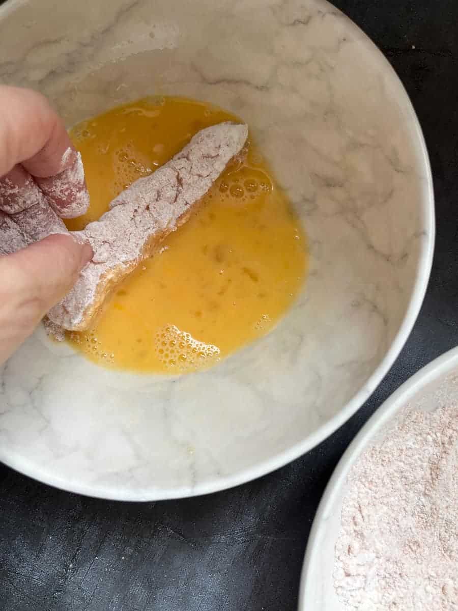 a fish finger being dipped into a bowl of beaten egg.