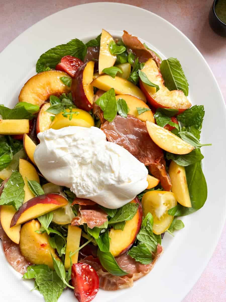 A green salad with sliced peaches, red and yellow tomatoes, grilled proscuitto and a ball of Burrata cheese ripped open to reveal the creamy middle.