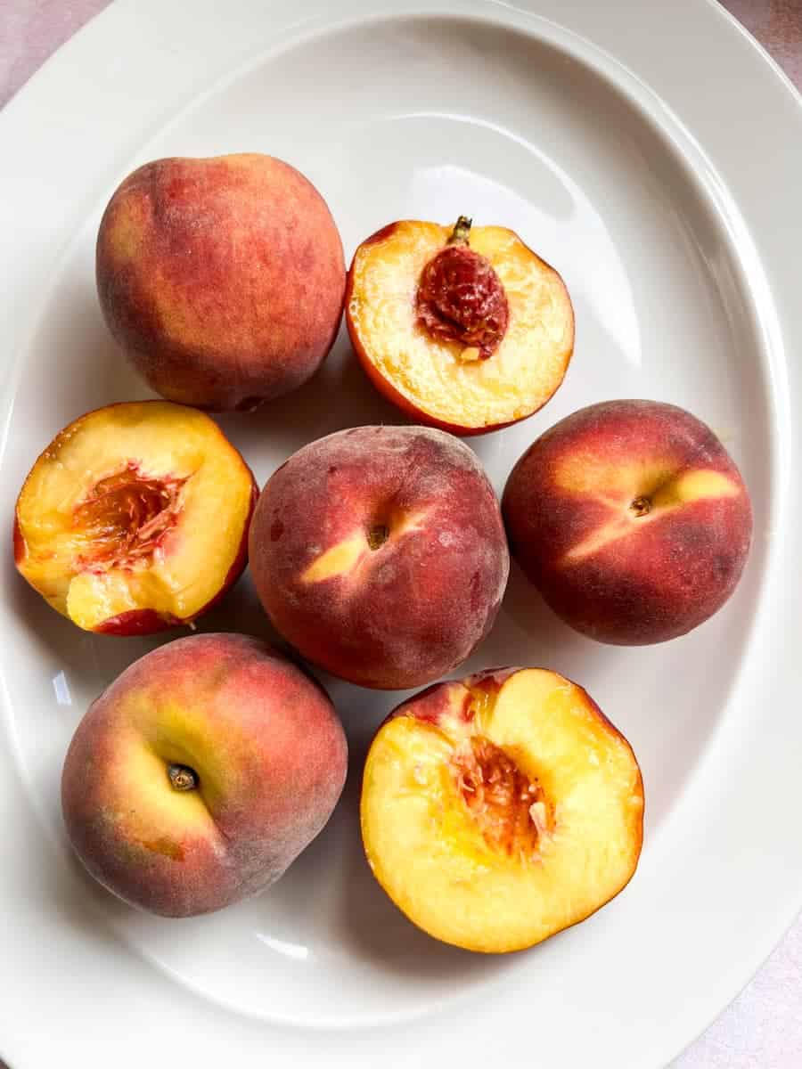 a white plate of fresh whole and halved peaches.
