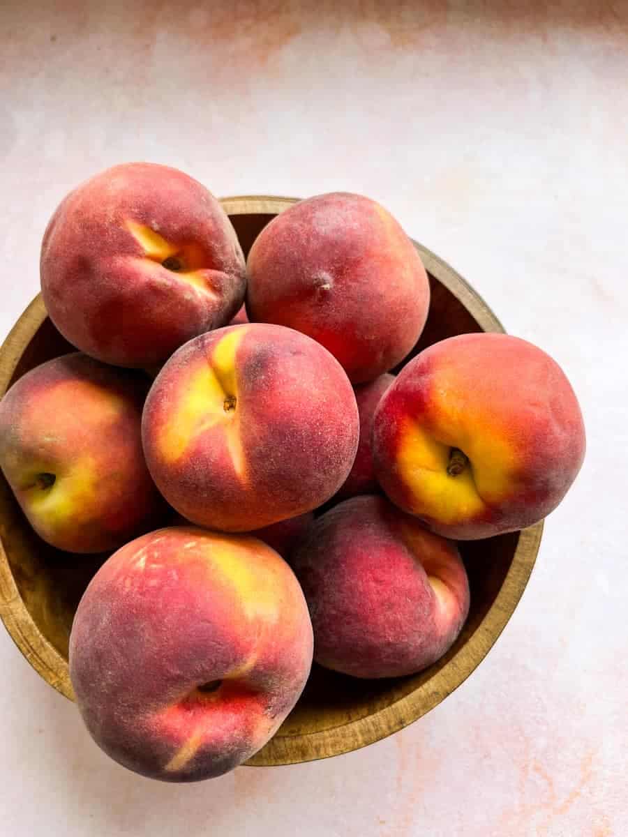 A wooden bowl filled with fresh peaches.