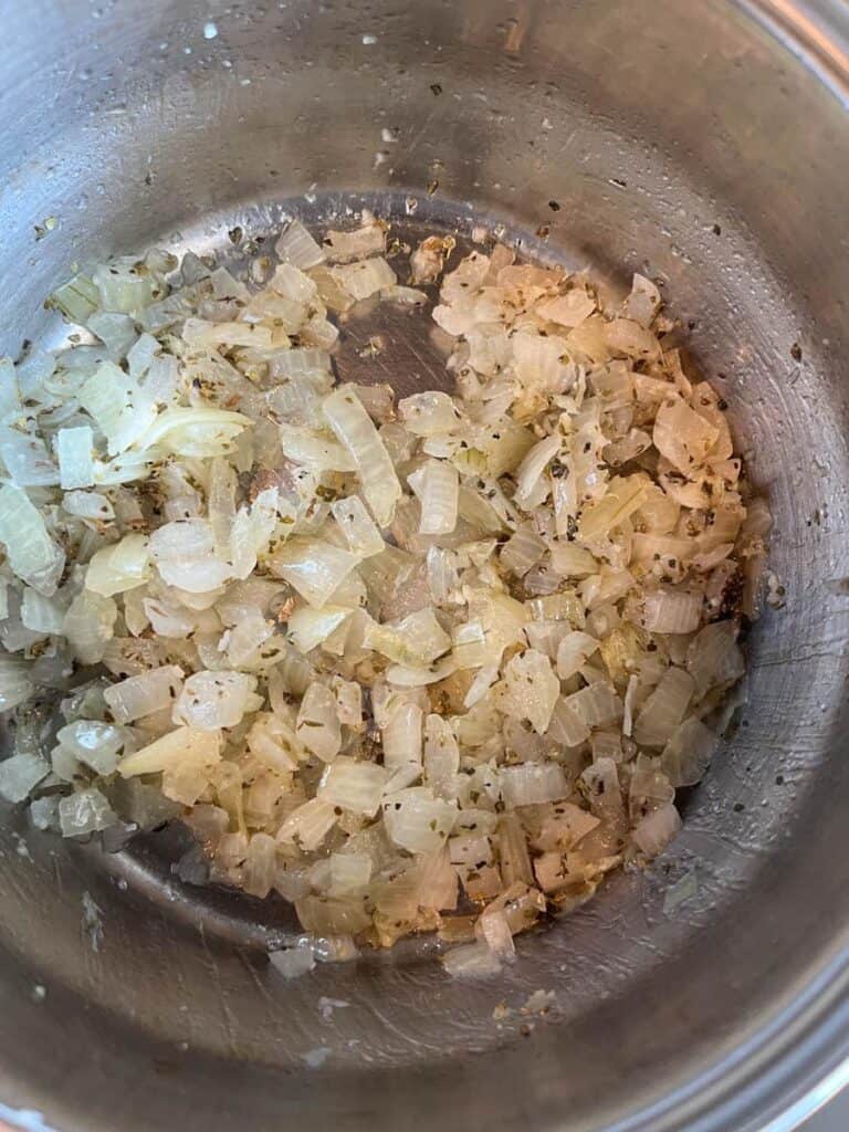 A silver saucepan of cooked onions with dried oregano.