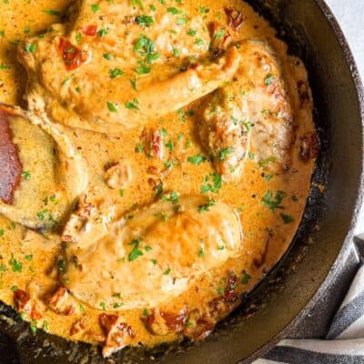 cooked chicken breasts in a sun dried tomato cream sauce with chopped parsley in a black skillet.