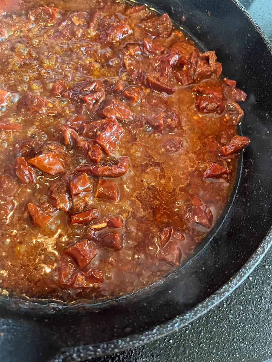 Chopped sun dried tomatoes and chicken stock in a black skillet.