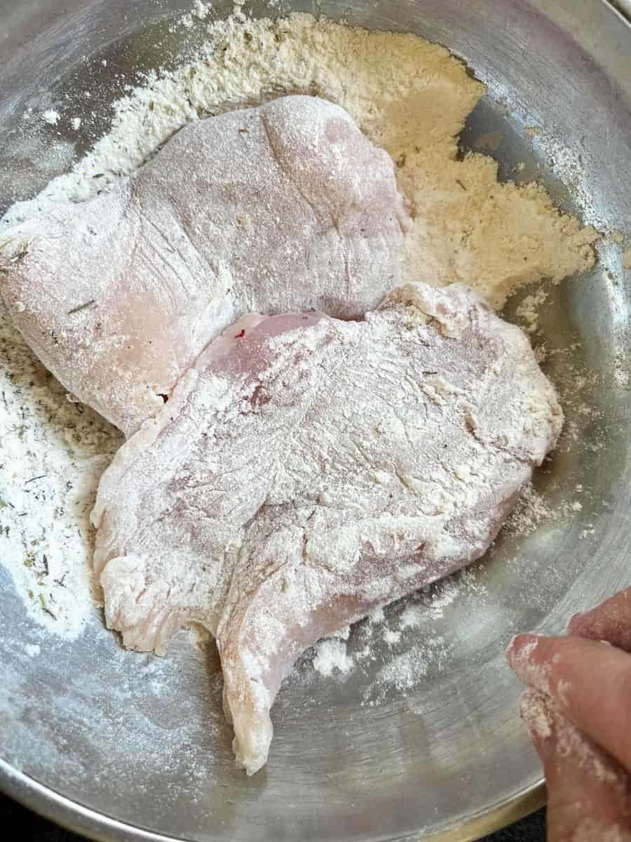 Chicken breasts in a silver bowl of flour.