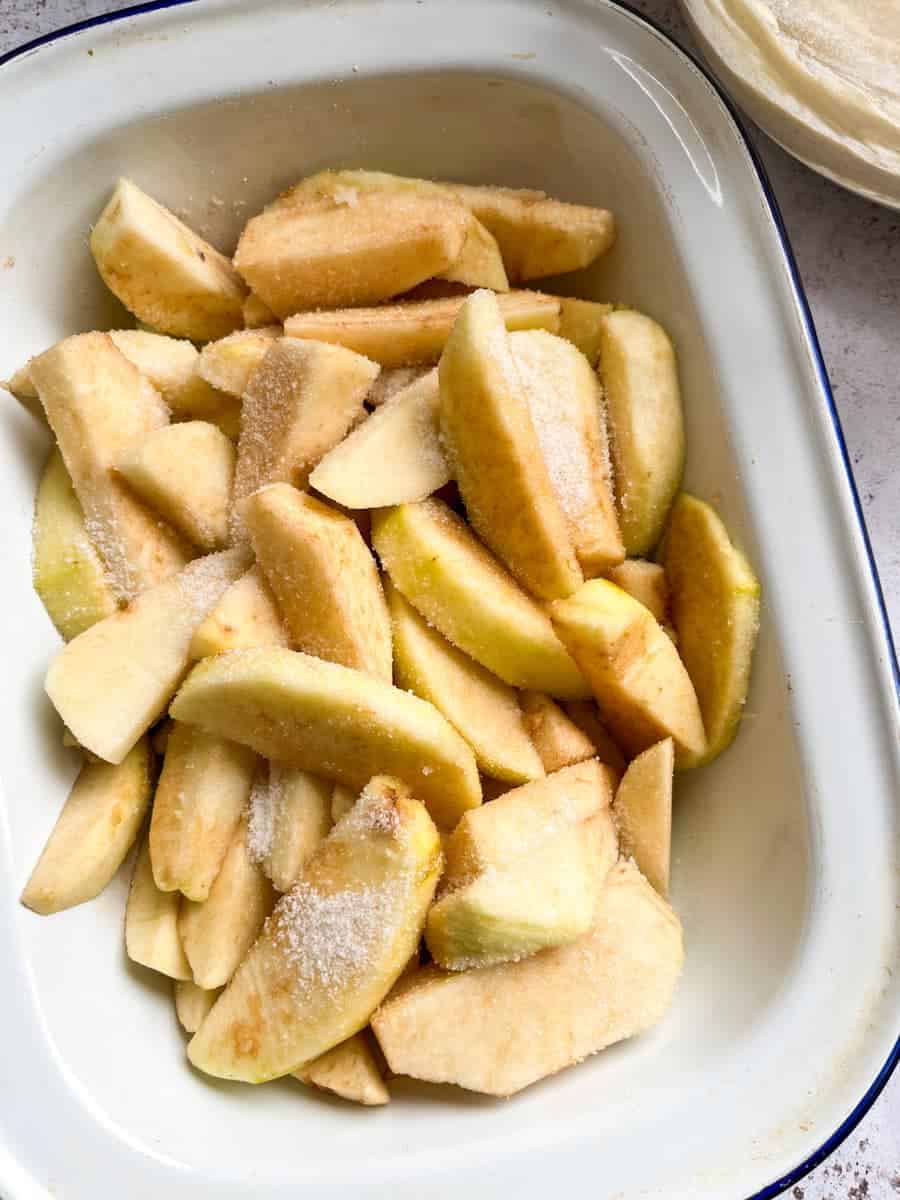 A blue and white enamel dish with sliced apples coated in cinnamon sugar.