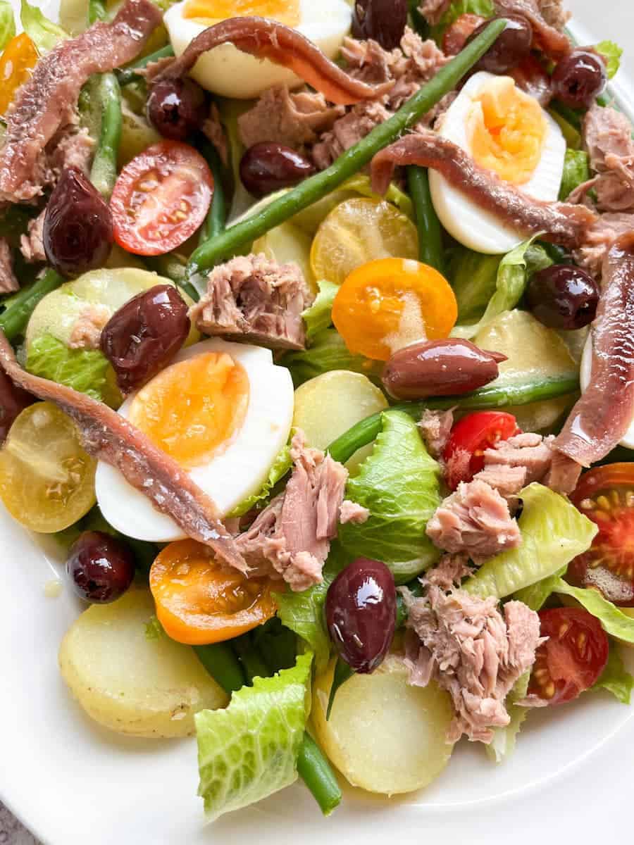 A salad with lettuce, tuna chunks, boiled eggs, anchovies, black olives, cherry tomatoes, potatoes and green beans.