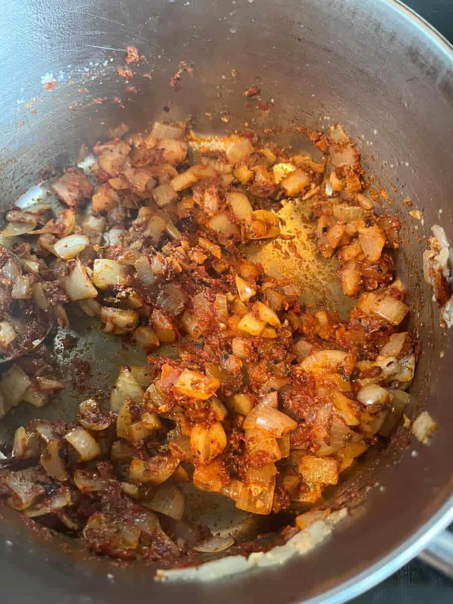 chopped onions and dried spices cooking in a silver pan.