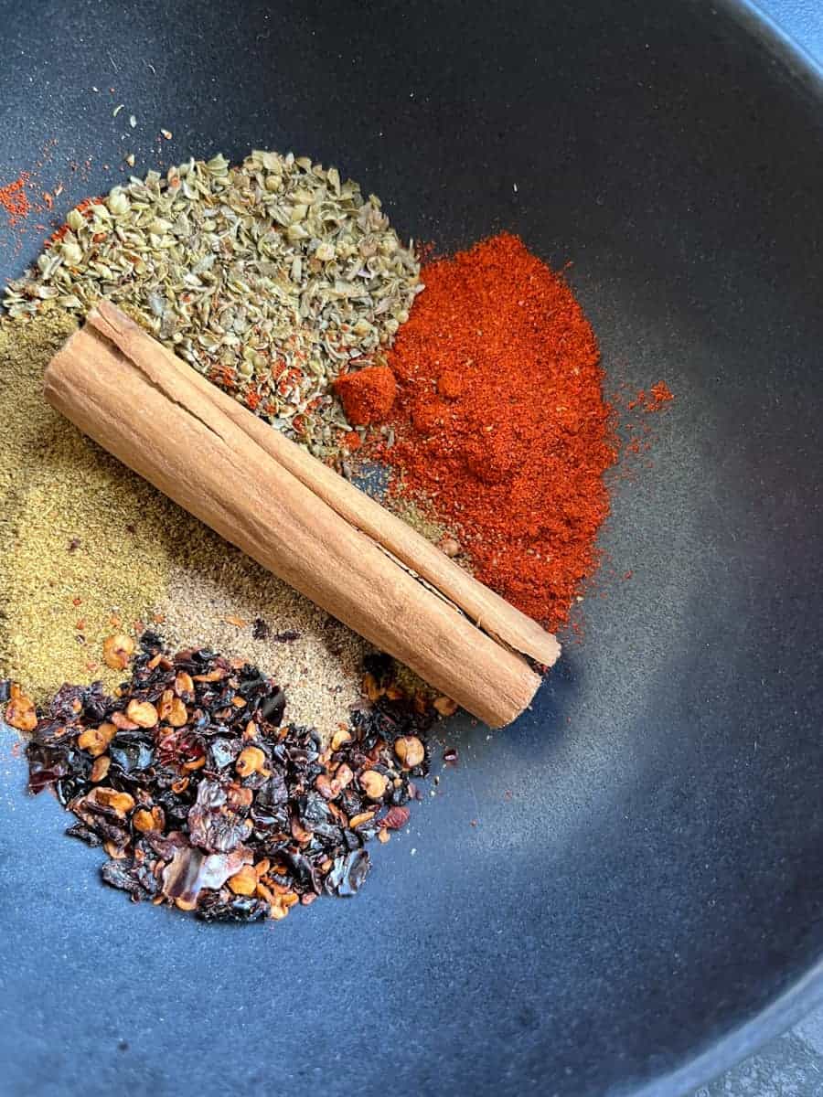 a black bowl with a cinnamon stick, crushed dried chillies, smoked paprika, cumin and oregano.