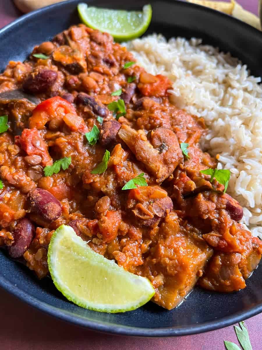 A bowl of aubergine and mushroom chilli with rice and lime wedges.