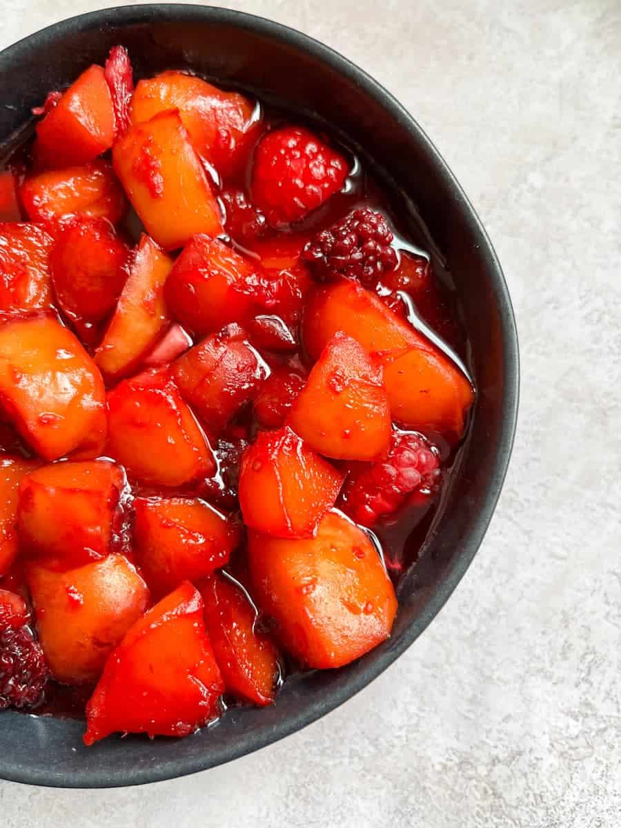 A black bowl of cooked peaches and blackberries.