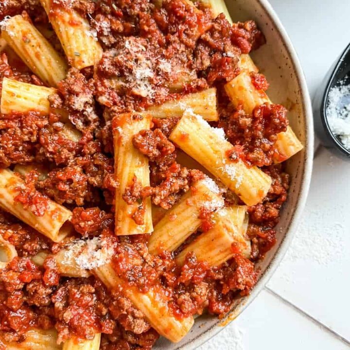 A bowl of tube pasta with ragu sauce and grated parmesan cheese.