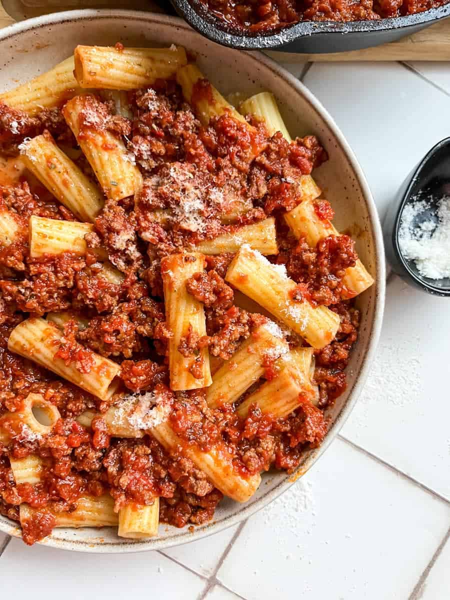 A bowl of rigatoni pasta with tomato ragu sprinkled with parmesan cheese.