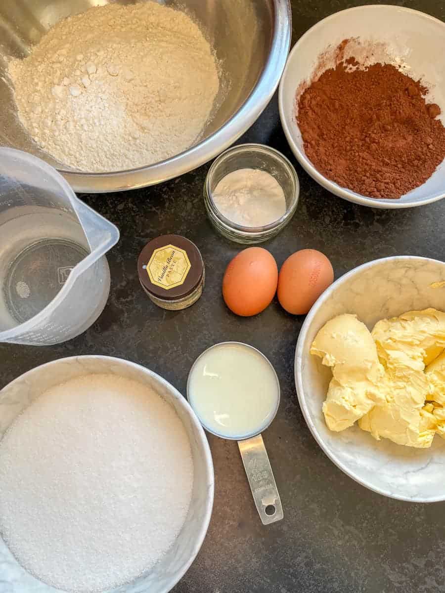 Bowls of ingredients such as butter, sugar, flour, cocoa powder, eggs, water and buttermilk to make a chocolate cake.