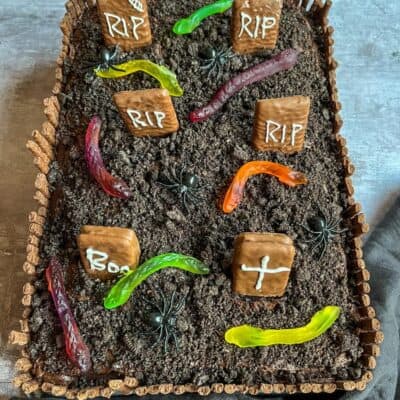 A Halloween chocolate Graveyard cake with crushed chocolate cookies for soil, candy worms, chocolate gravestones and spider decorations.