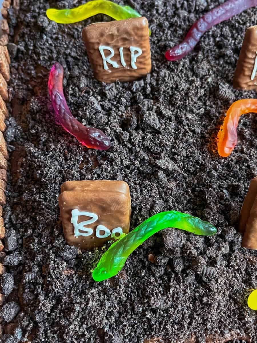 A Halloween cake with crushed chocolate cookies to resemble dirt, candy worms and chocolate gravestones.