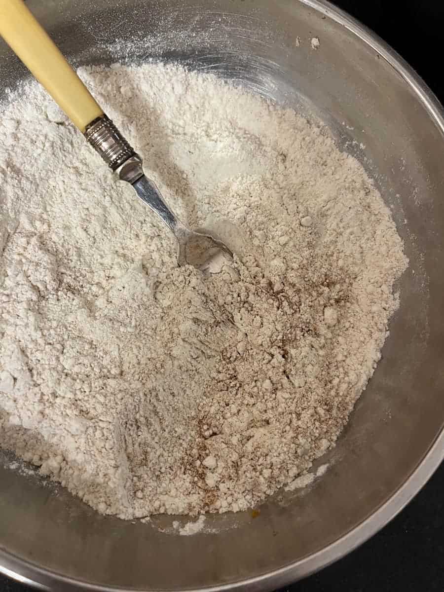 A silver bowl of flour and ground cinnamon with a yellow handled fork.