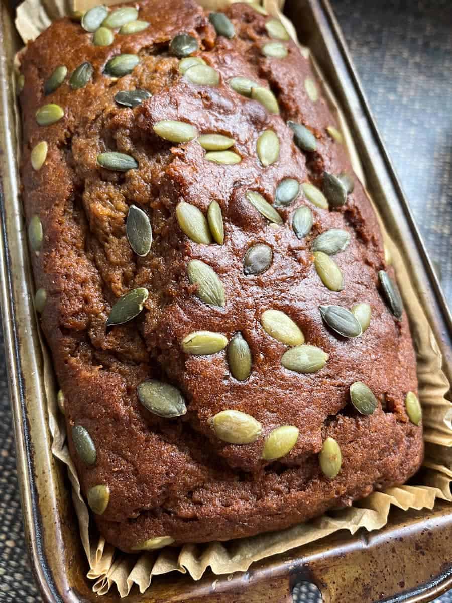 Pumpkin bread scattered with pumpkin seeds in a loaf tin.