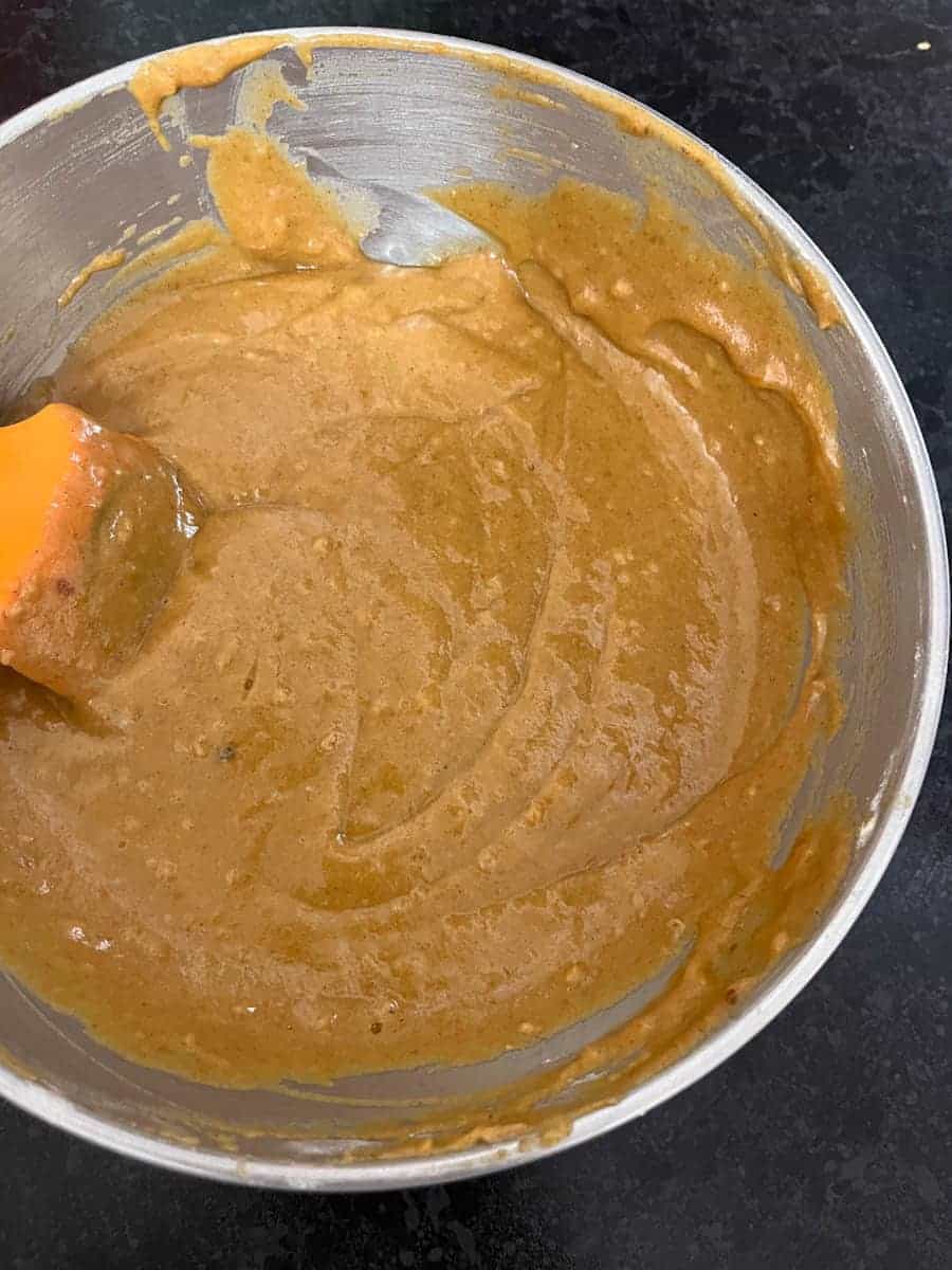 A silver bowl of pumpkin cake batter with an orange spatula.