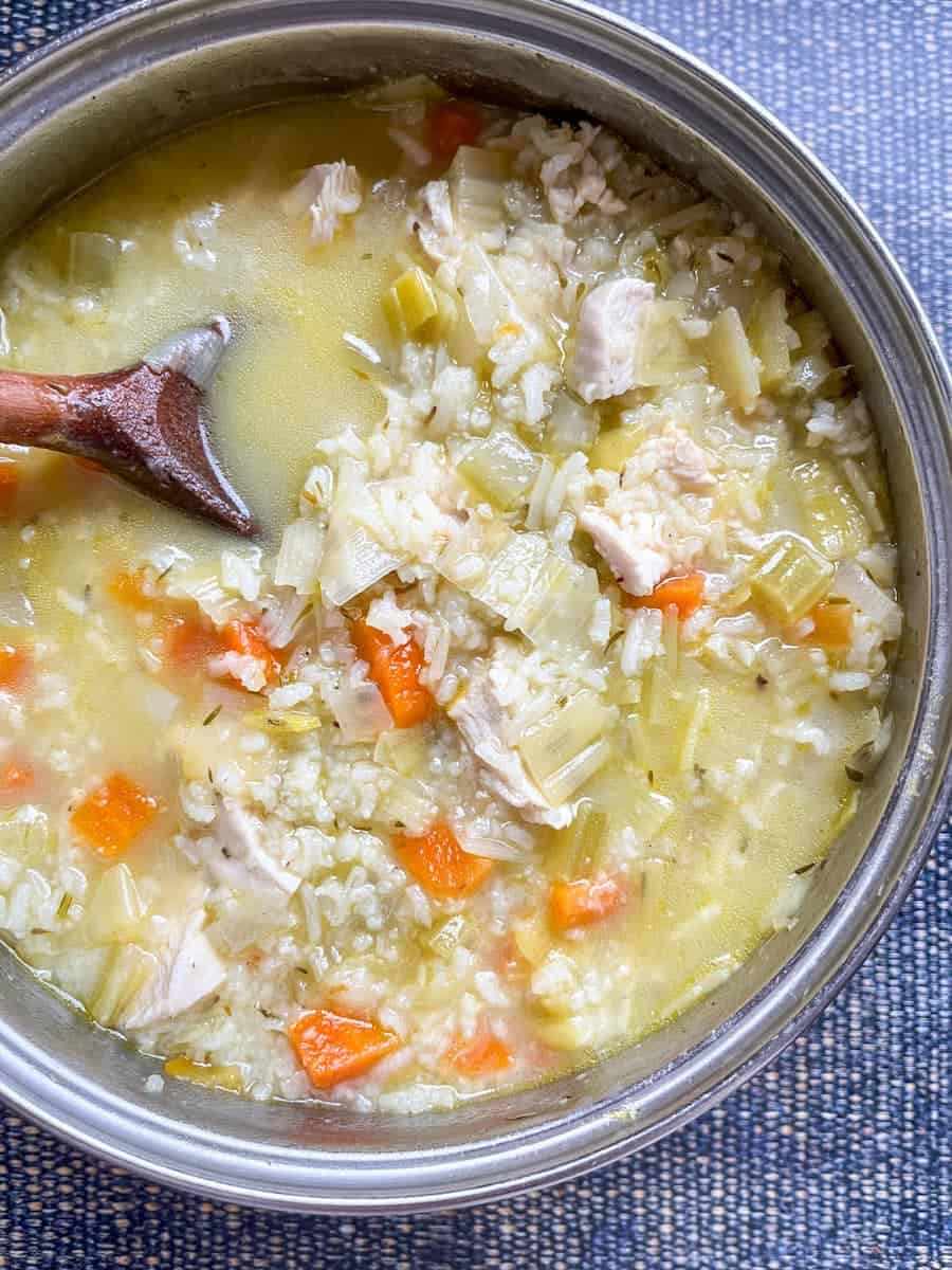 A silver pan of chicken and rice soup with diced carrots and leeks.