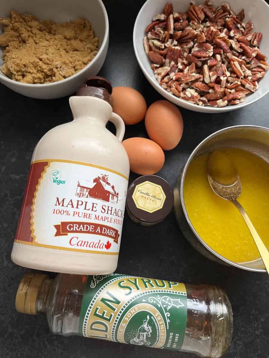 A collection of ingredients such as pecans, brown sugar, eggs and bottles of syrup to make pecan pie.