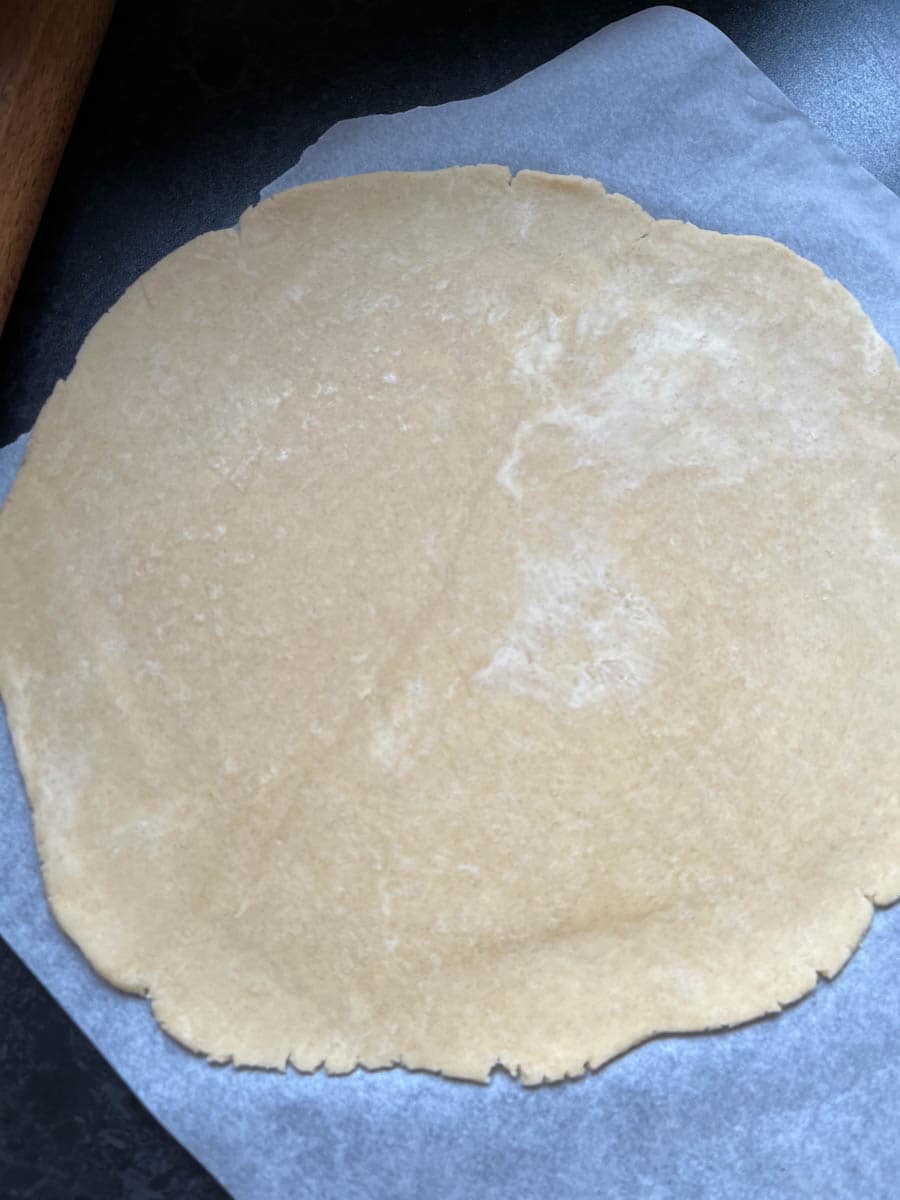 Pie crust dough rolled out into a large circle on a piece of baking paper.