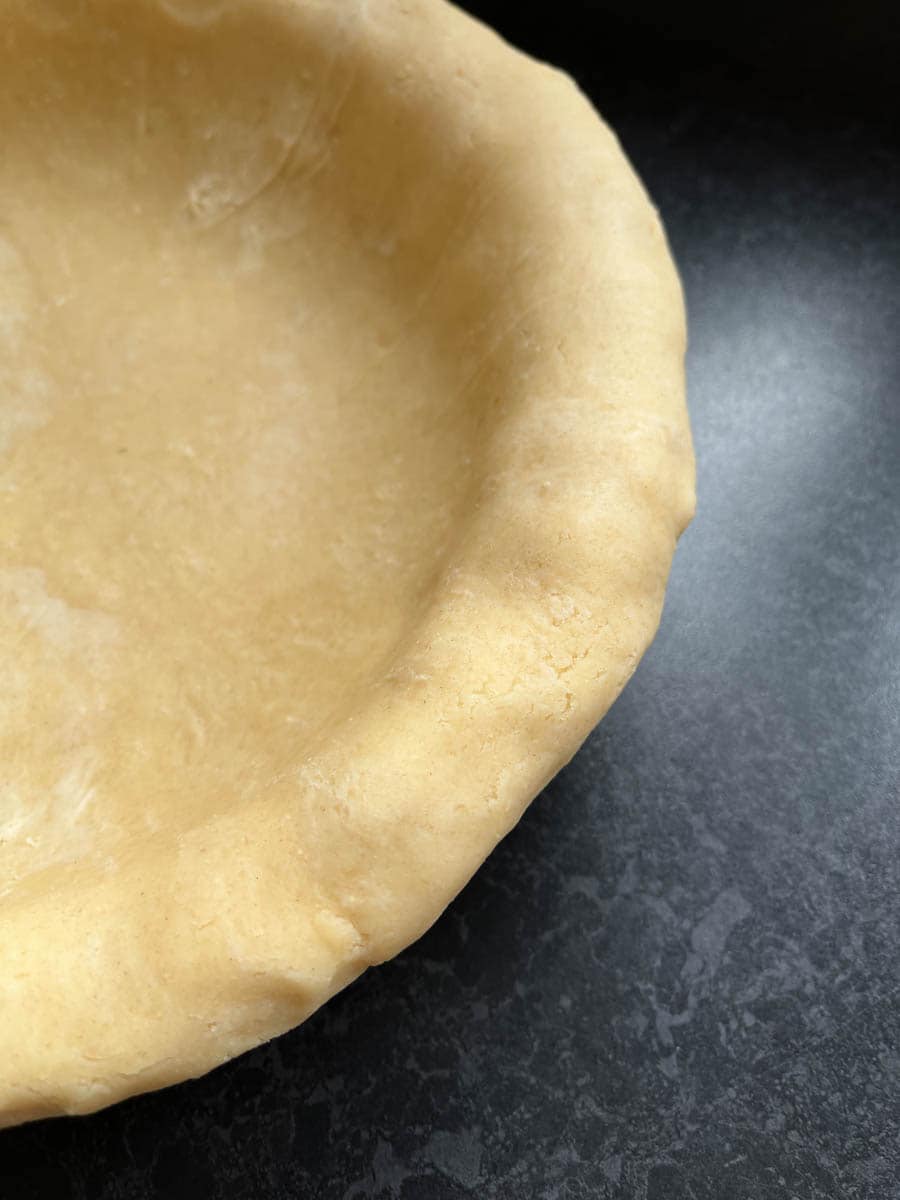 An unbaked pie crust on a black and grey work surface.
