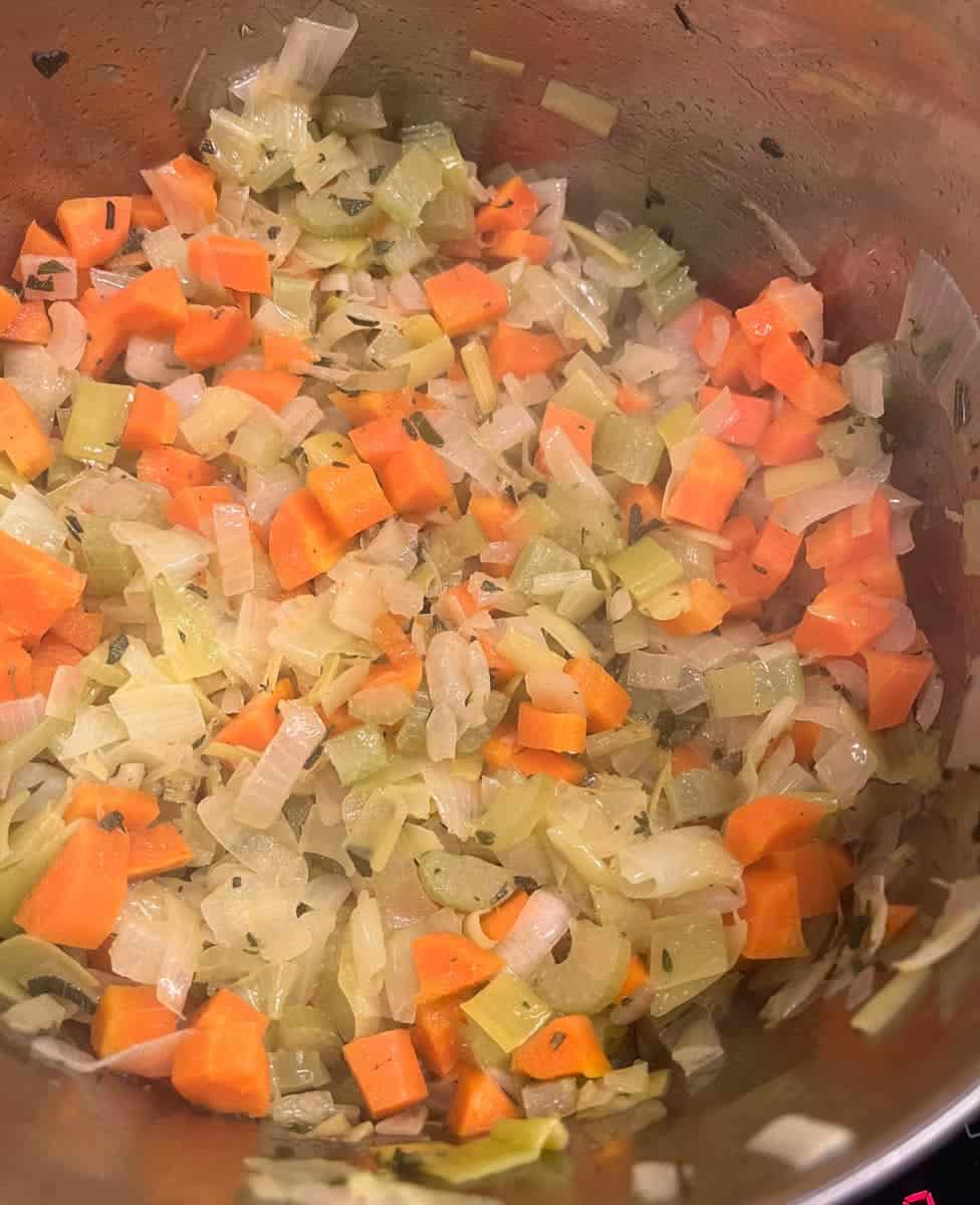 Cooked chopped carrots, onion, fresh herbs and celery in a silver saucepan.