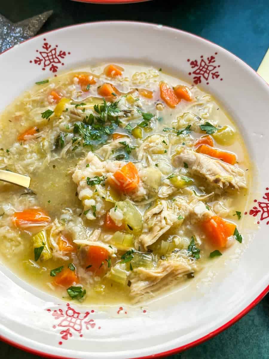 A red and white bowl of turkey soup with celery, carrots and chopped parsley.