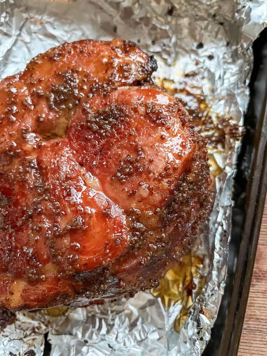 A piece of gammon covered in a mustard and maple syrup glaze on a baking tray lined with tin foil.