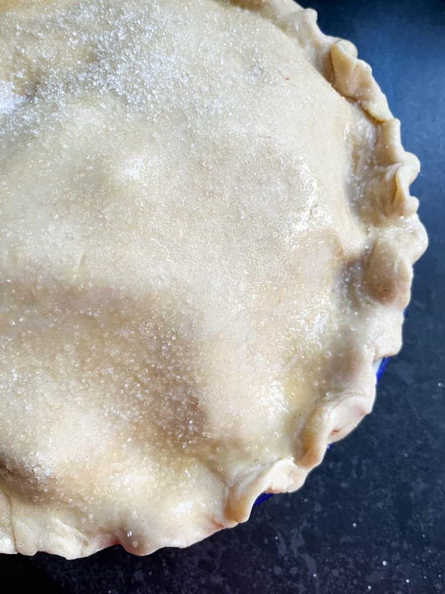 An unbaked pie with crimped edges and sprinkled with sugar.