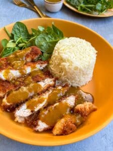 A yellow bowl of breaded chicken strips with a Katsu curry sauce, white rice and a green salad.