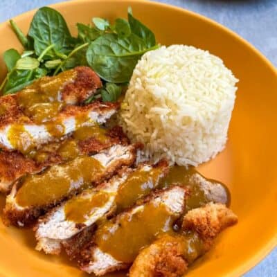 A yellow bowl of breaded chicken strips with a Katsu curry sauce, white rice and a green salad.