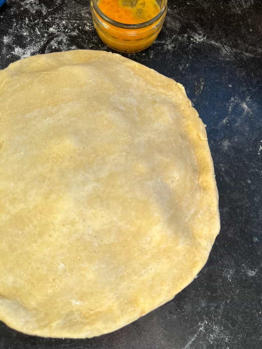 A piece of pie dough placed over a pie dish and a small jar of beaten egg.